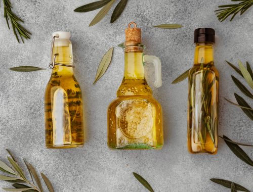 Glass bottle with olive oil on gray background, top view